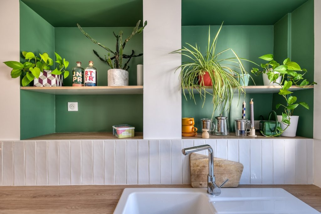 Cuisine ouverte sur le séjour avec plan de travail en bois, crédence claire et niches murales peintes en vert