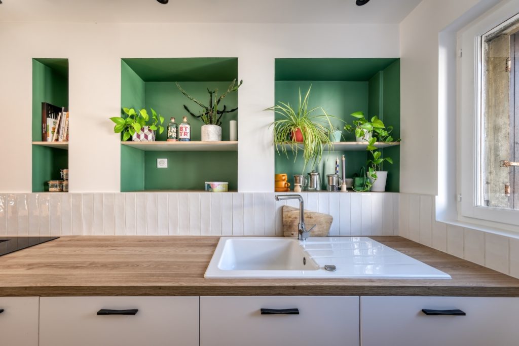 Cuisine ouverte sur le séjour avec plan de travail en bois, crédence claire et niches murales peintes en vert