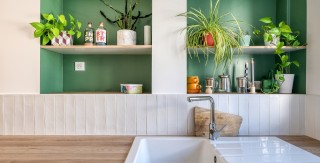 Cuisine ouverte sur le séjour avec plan de travail en bois, crédence claire et niches murales peintes en vert